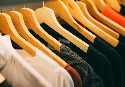 pexels-photo-996329-996329 A close-up view of a row of clothes on wooden hangers, showcasing various fabrics and colors in a wardrobe setting.